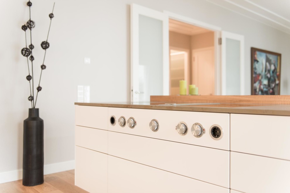 Photo of a large contemporary single-wall open plan kitchen in Berlin with flat-panel cabinets, white cabinets, quartz worktops, white splashback, glass sheet splashback, stainless steel appliances, medium hardwood flooring, an island, beige floors, brown worktops and a submerged sink.