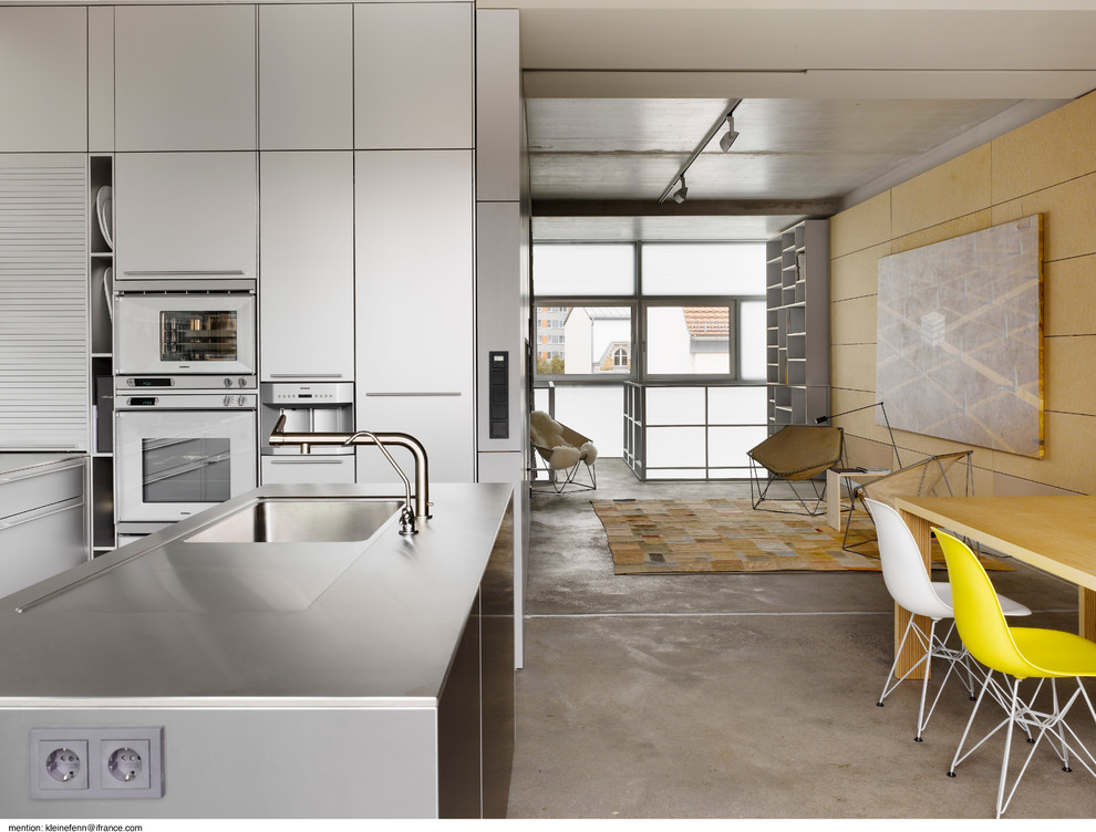 Cette image montre une cuisine ouverte design en inox avec un évier encastré, un placard à porte plane, un plan de travail en inox, un électroménager en acier inoxydable, sol en béton ciré et îlot.