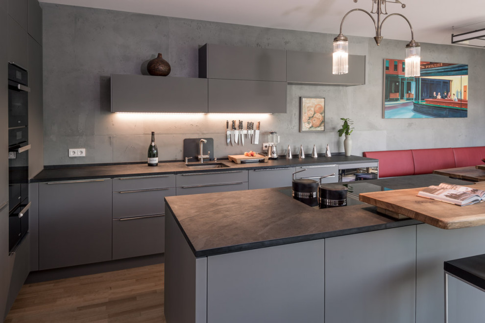 Inspiration for a large contemporary l-shaped open plan kitchen in Dresden with flat-panel cabinets, grey cabinets, wood worktops, grey splashback, black appliances, light hardwood flooring, an island, brown floors and brown worktops.