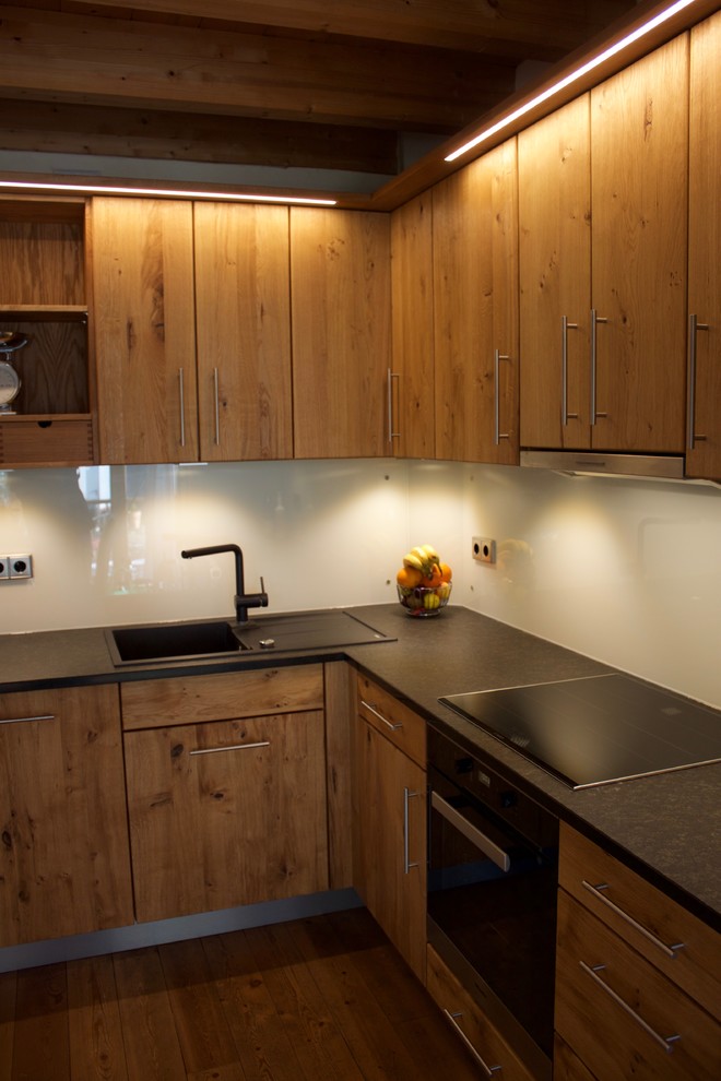 Пример оригинального дизайна: угловая кухня-гостиная среднего размера в современном стиле с одинарной мойкой, гранитной столешницей, белым фартуком, фартуком из стекла, техникой из нержавеющей стали и светлым паркетным полом
