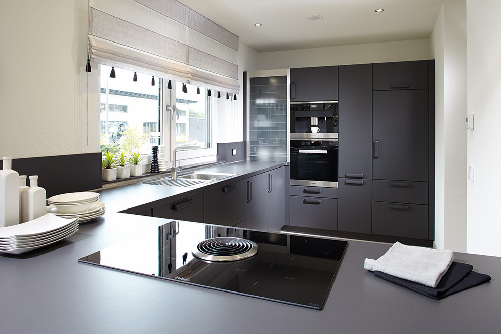 Immagine di una cucina contemporanea con ante grigie, paraspruzzi grigio, elettrodomestici neri, penisola e top grigio