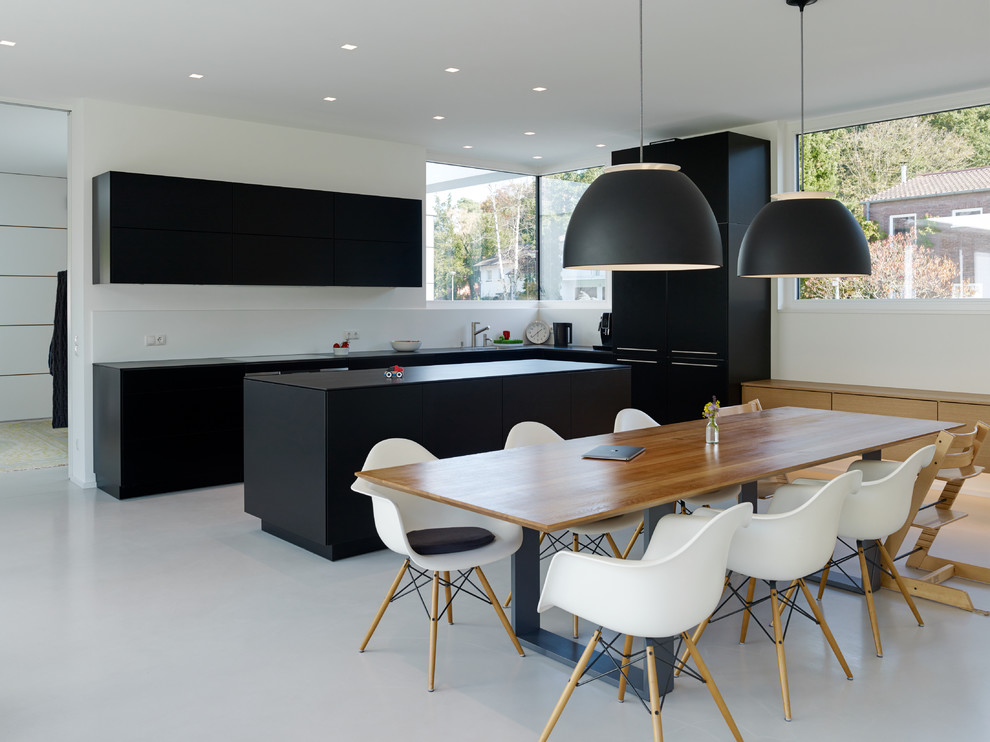 Große Moderne Wohnküche in L-Form mit weißem Boden, flächenbündigen Schrankfronten, schwarzen Schränken, Küchenrückwand in Weiß, schwarzen Elektrogeräten, Betonboden und Kücheninsel in Sonstige