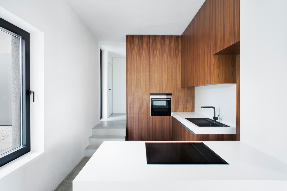 Small modern enclosed kitchen in Berlin with flat-panel cabinets, medium wood cabinets, a breakfast bar, a built-in sink, white splashback, integrated appliances, concrete flooring and grey floors.