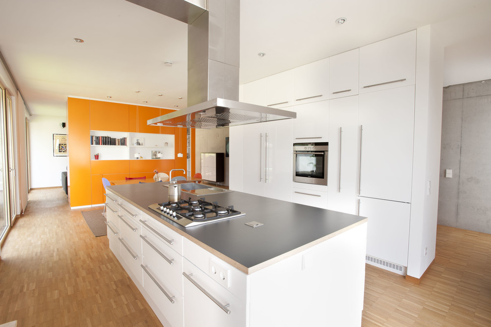 Large contemporary kitchen/diner in Frankfurt with a built-in sink, flat-panel cabinets, white cabinets, integrated appliances, light hardwood flooring and an island.