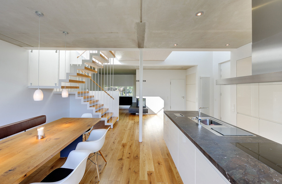 Große, Offene Moderne Küche mit flächenbündigen Schrankfronten, weißen Schränken, braunem Holzboden, Kücheninsel und Einbauwaschbecken in Berlin