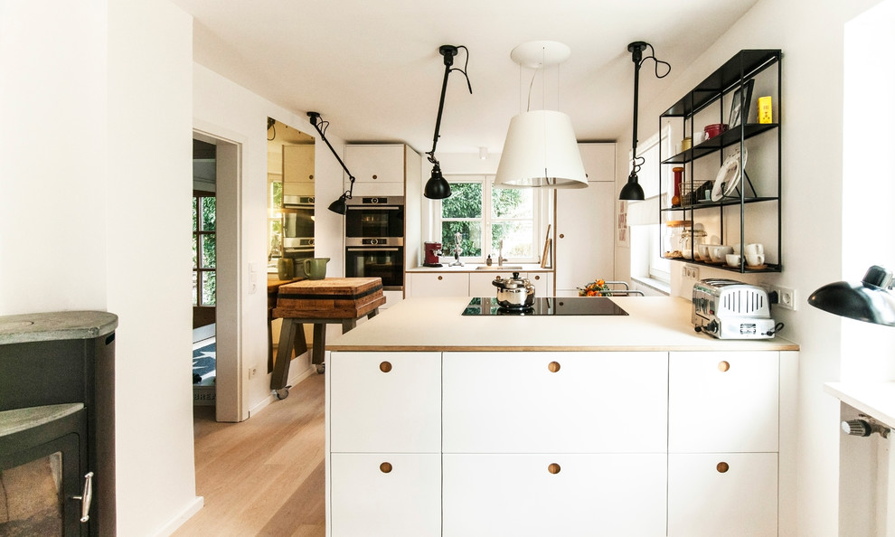 Open concept kitchen - mid-sized contemporary u-shaped light wood floor and brown floor open concept kitchen idea in Munich with a drop-in sink, flat-panel cabinets, white cabinets, white backsplash, a peninsula, black appliances and white countertops