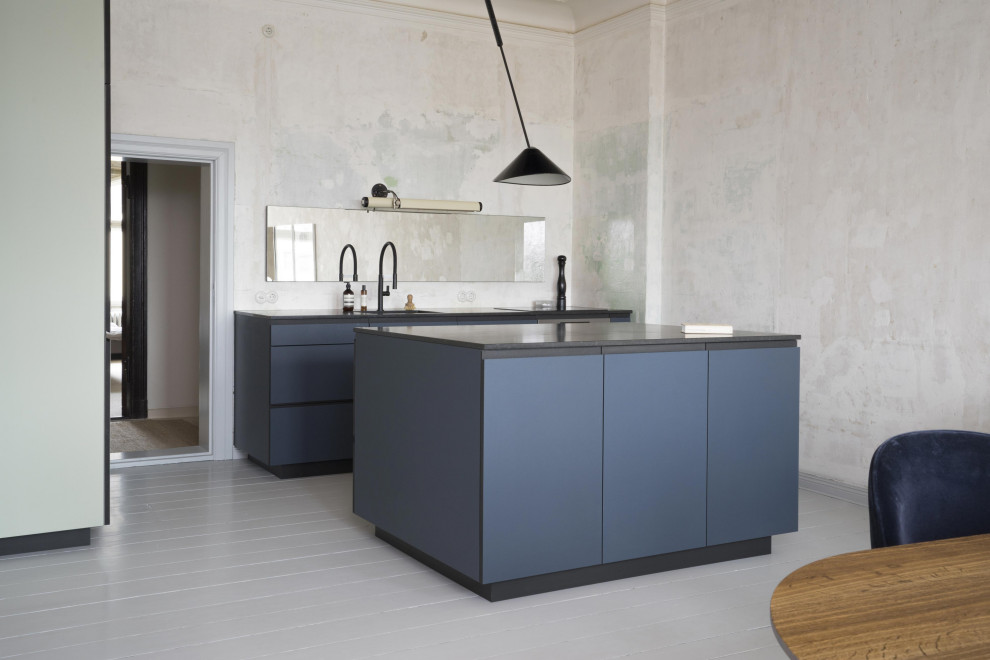 This is an example of a medium sized modern single-wall kitchen/diner in Berlin with a built-in sink, flat-panel cabinets, blue cabinets, granite worktops, integrated appliances, light hardwood flooring, an island, white floors and black worktops.
