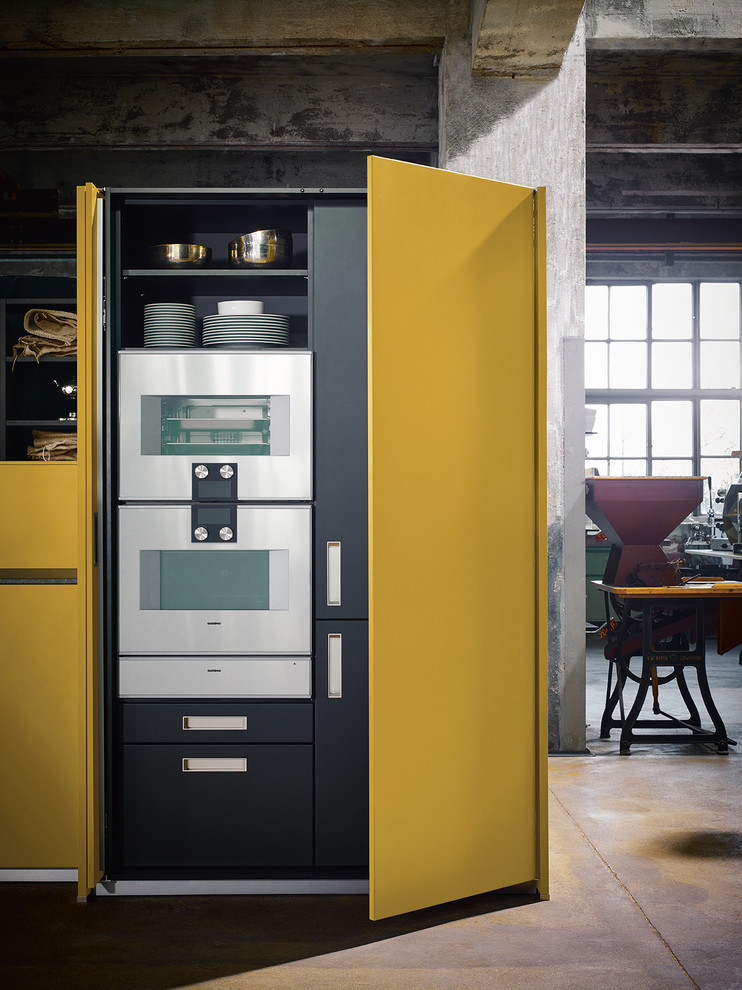 ニュルンベルクにあるコンテンポラリースタイルのおしゃれなキッチン (フラットパネル扉のキャビネット、黄色いキャビネット、シルバーの調理設備、茶色いキッチンカウンター) の写真