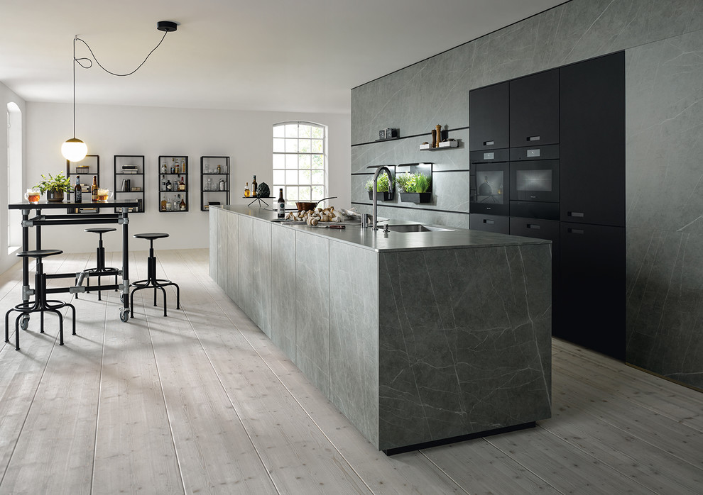 Design ideas for an urban galley open plan kitchen in Nuremberg with flat-panel cabinets, grey cabinets, black appliances, grey worktops, an island and grey splashback.