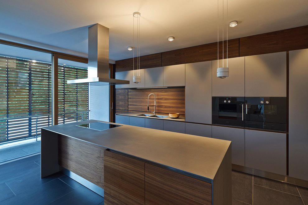 Стильный дизайн: прямая кухня среднего размера в современном стиле с накладной мойкой, плоскими фасадами, серыми фасадами, коричневым фартуком, черной техникой и островом - последний тренд