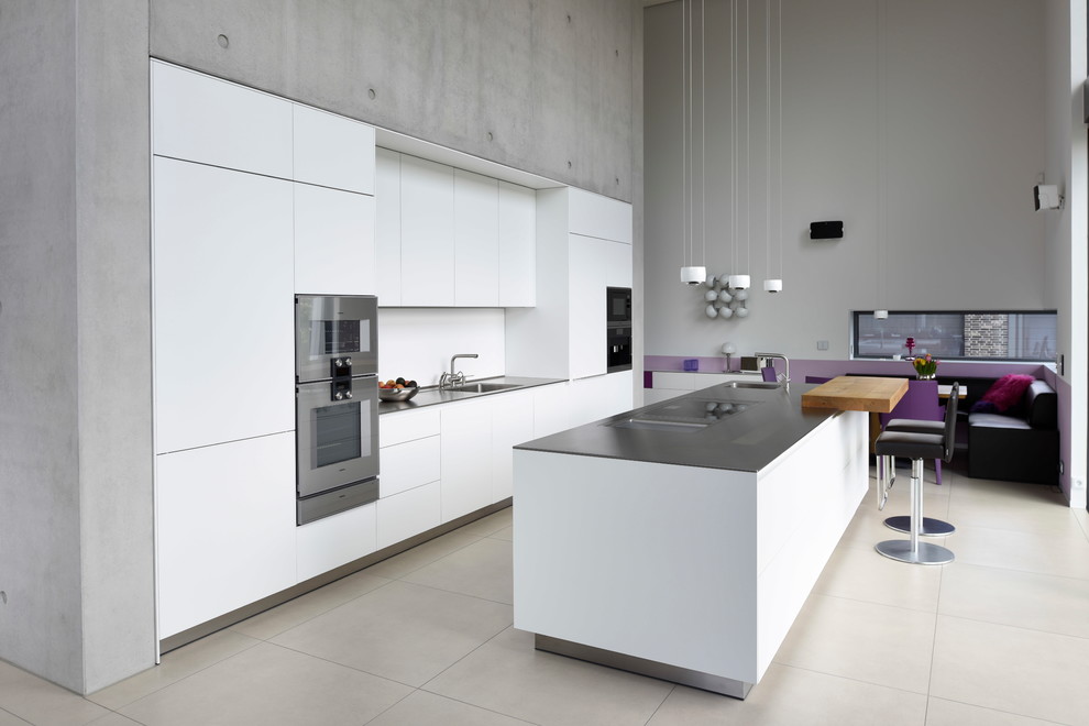 Modern inredning av ett grå grått kök och matrum, med en enkel diskho, släta luckor, vita skåp, vitt stänkskydd, rostfria vitvaror, en köksö och beiget golv