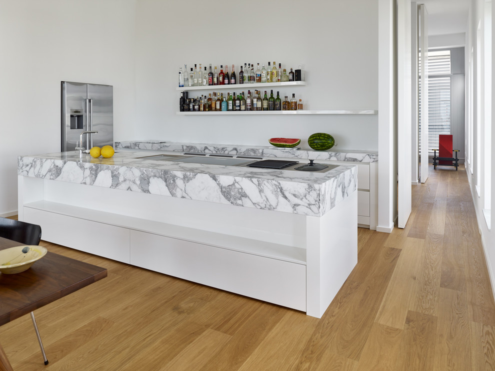 Offene, Einzeilige Moderne Küche mit integriertem Waschbecken, weißen Schränken, Marmor-Arbeitsplatte, Küchengeräten aus Edelstahl, braunem Holzboden, Kücheninsel, flächenbündigen Schrankfronten und Küchenrückwand in Weiß in Frankfurt am Main