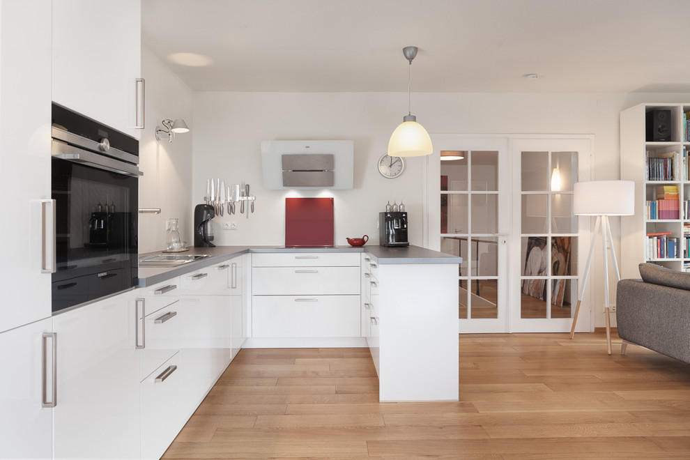 Идея дизайна: п-образная кухня-гостиная в скандинавском стиле с накладной мойкой, белыми фасадами, красным фартуком, черной техникой, светлым паркетным полом и полуостровом