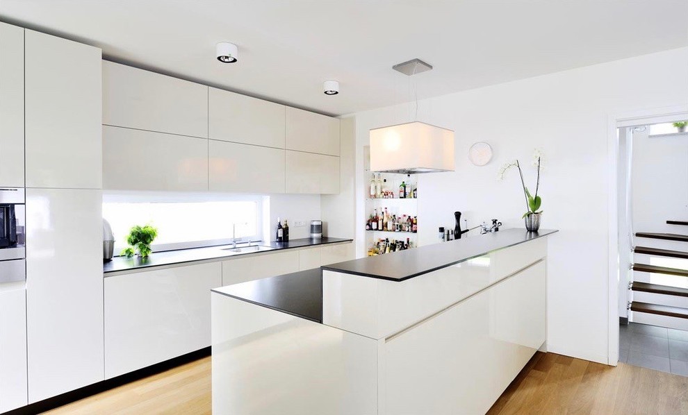 Immagine di una grande cucina moderna con ante bianche, paraspruzzi bianco, elettrodomestici in acciaio inossidabile, lavello integrato, ante lisce, parquet chiaro e pavimento marrone
