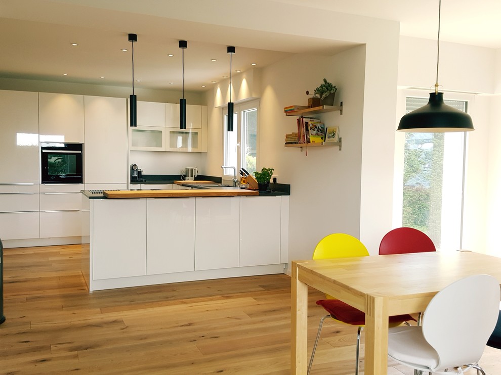 Photo of a medium sized classic u-shaped open plan kitchen in Dusseldorf with flat-panel cabinets, white cabinets, granite worktops, white splashback, a breakfast bar and black worktops.