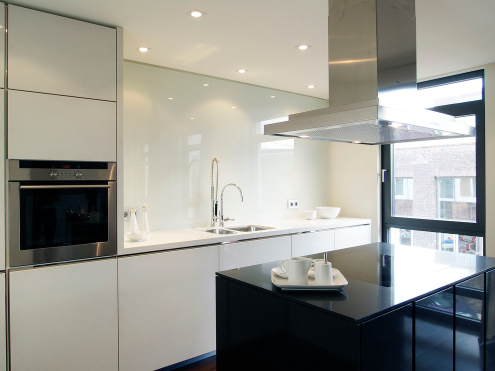 Foto på ett avskilt, mellanstort funkis linjärt kök, med en dubbel diskho, släta luckor, vita skåp, vitt stänkskydd, glaspanel som stänkskydd, integrerade vitvaror och en köksö