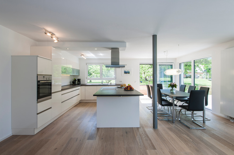 Свежая идея для дизайна: угловая кухня-гостиная в современном стиле с плоскими фасадами, белыми фасадами, паркетным полом среднего тона и островом - отличное фото интерьера