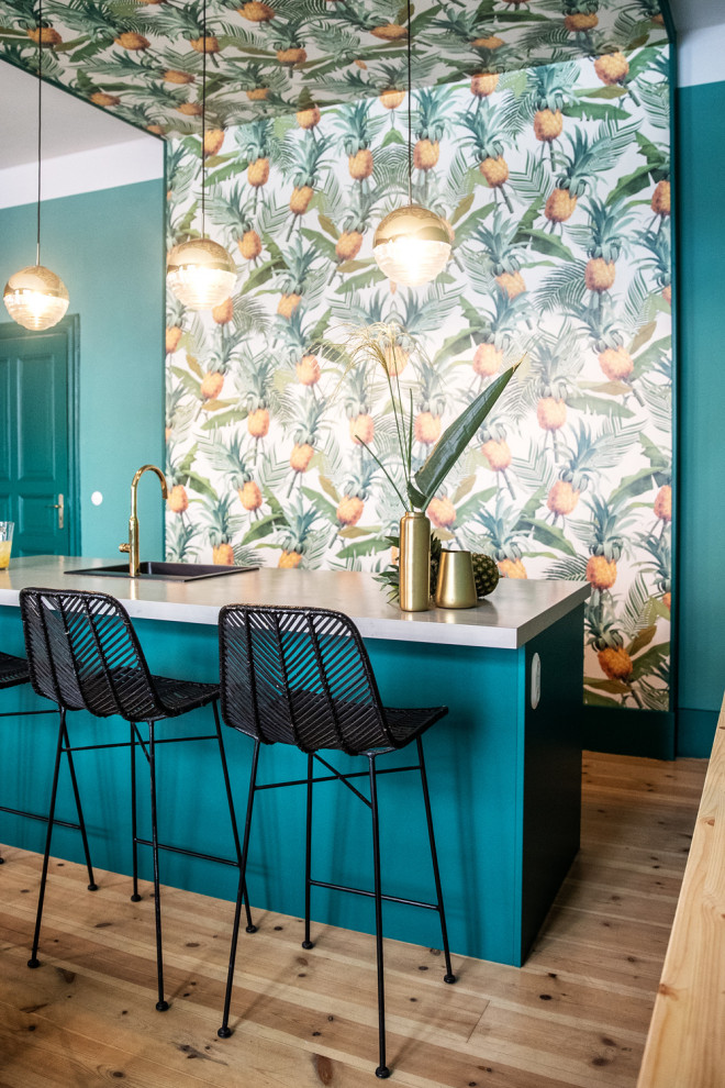 Diseño de cocina contemporánea con fregadero de un seno, encimera de cemento, salpicadero azul, suelo de madera clara, una isla, suelo marrón y papel pintado