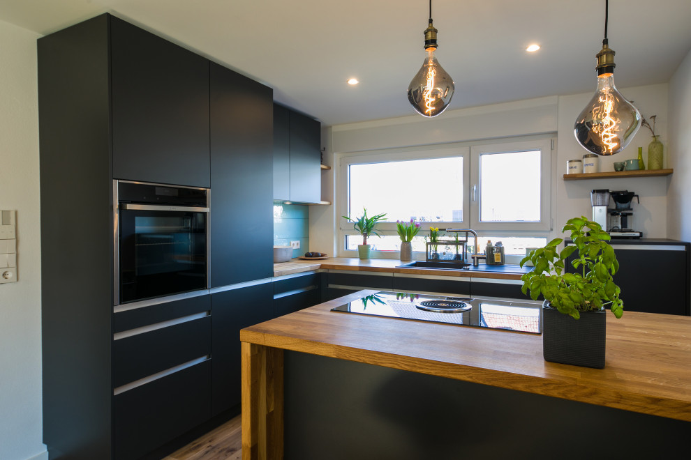 Immagine di una cucina design di medie dimensioni con ante lisce, ante nere, top in legno e penisola
