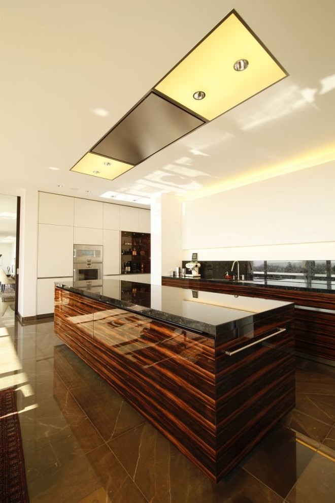 Ejemplo de cocina actual extra grande abierta con electrodomésticos de acero inoxidable, armarios con paneles lisos, salpicadero negro y una isla