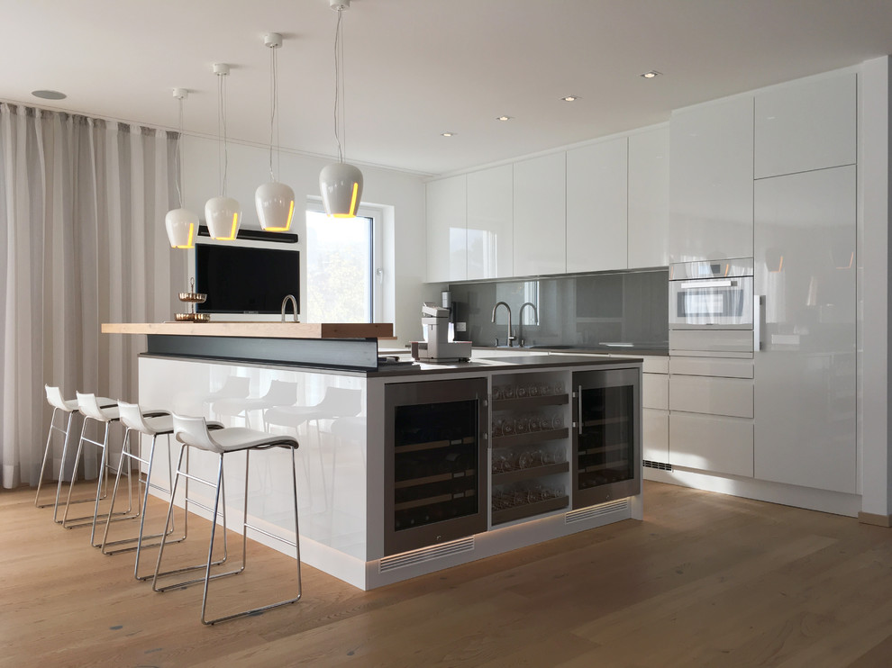 Mid-sized trendy l-shaped brown floor and medium tone wood floor open concept kitchen photo in Munich with flat-panel cabinets, white cabinets, wood countertops, gray backsplash, white appliances and an island