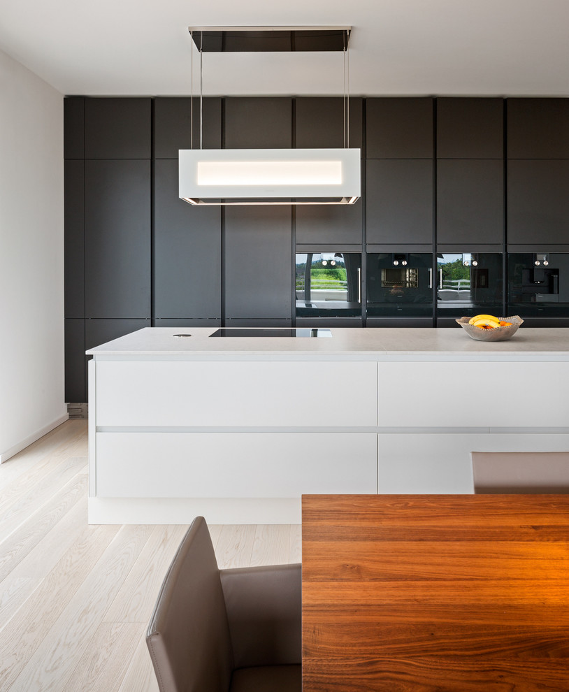 Идея дизайна: большая серо-белая кухня-гостиная в современном стиле с плоскими фасадами, черными фасадами, черной техникой, светлым паркетным полом и островом