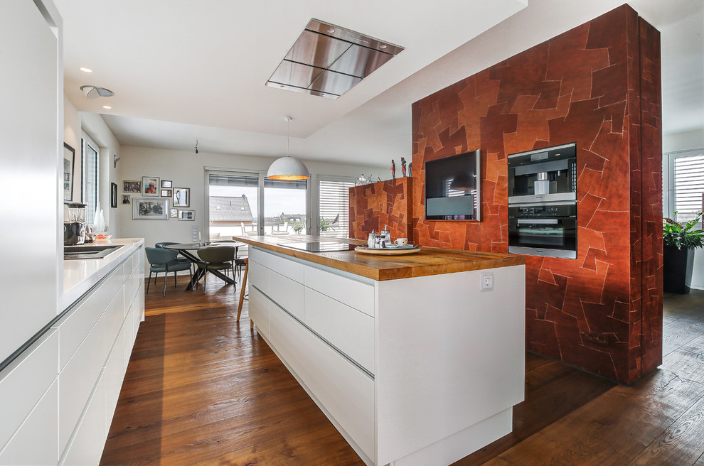 Offene, Zweizeilige Moderne Küche mit flächenbündigen Schrankfronten, weißen Schränken, schwarzen Elektrogeräten, dunklem Holzboden und Kücheninsel in Köln