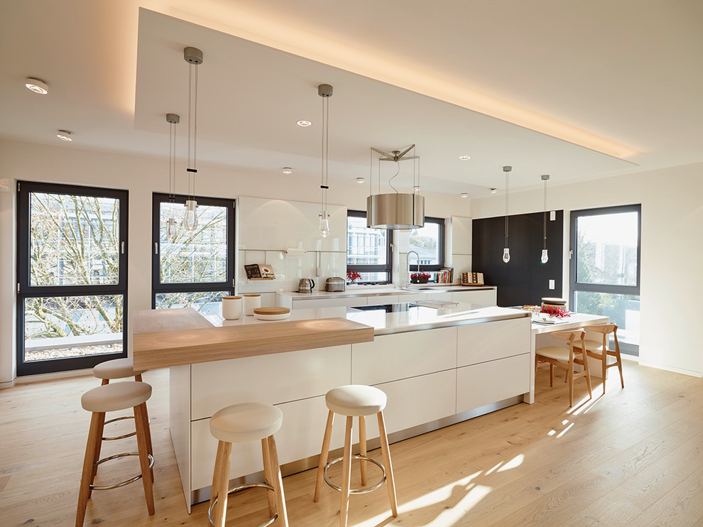 Große Moderne Wohnküche in L-Form mit flächenbündigen Schrankfronten, Küchenrückwand in Weiß, Glasrückwand, hellem Holzboden und Kücheninsel in Frankfurt am Main