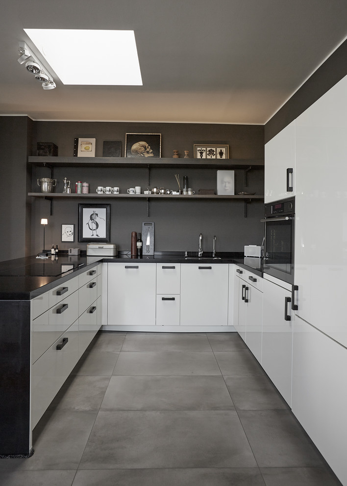 Small contemporary u-shaped open plan kitchen in Berlin with a built-in sink, flat-panel cabinets, white cabinets, brown splashback, stainless steel appliances, concrete flooring, a breakfast bar, grey floors and black worktops.