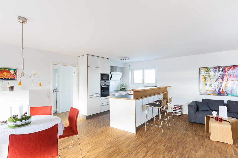 Medium sized contemporary single-wall open plan kitchen in Stuttgart with a built-in sink, flat-panel cabinets, white cabinets, laminate countertops, stainless steel appliances, an island and grey worktops.