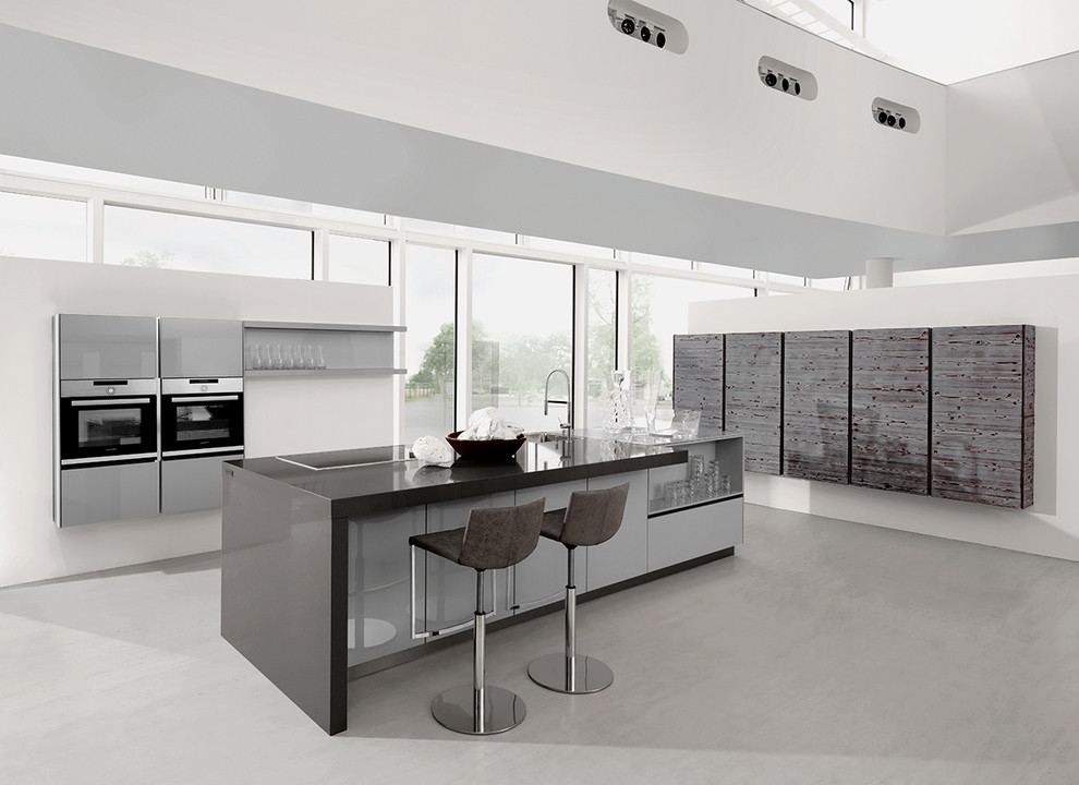 Large minimalist galley concrete floor and gray floor open concept kitchen photo in Frankfurt with flat-panel cabinets, gray cabinets, quartz countertops, an island, a drop-in sink, white backsplash, window backsplash, stainless steel appliances and black countertops