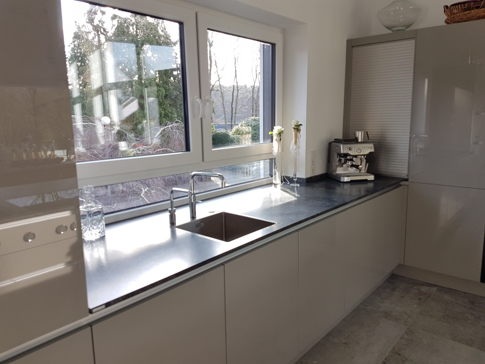 This is an example of an expansive contemporary l-shaped open plan kitchen in Dortmund with a built-in sink, glass-front cabinets, grey cabinets, granite worktops, black appliances, an island and grey worktops.