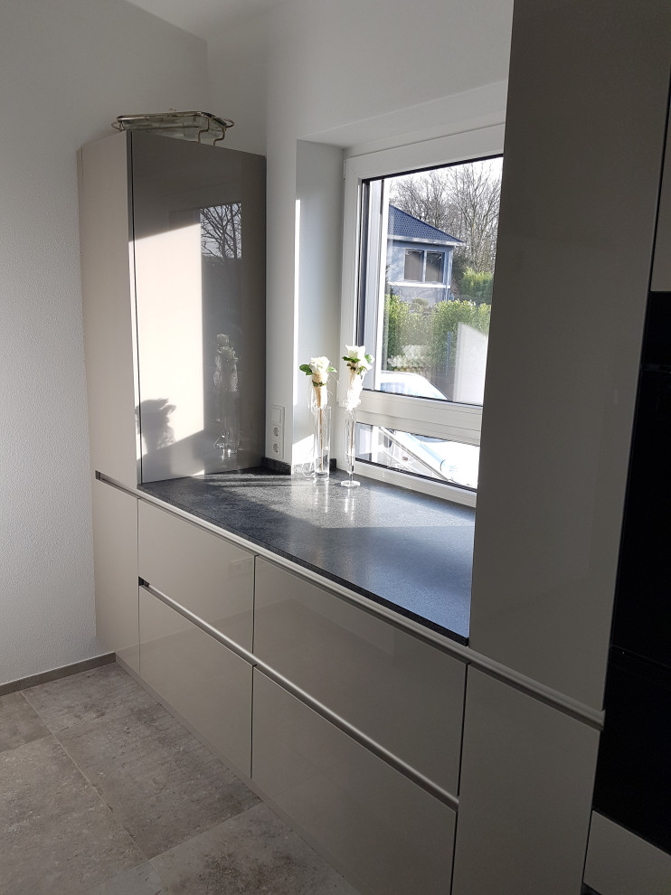 Modern inredning av ett mycket stort grå grått kök, med en nedsänkt diskho, luckor med glaspanel, grå skåp, granitbänkskiva, svarta vitvaror och en köksö