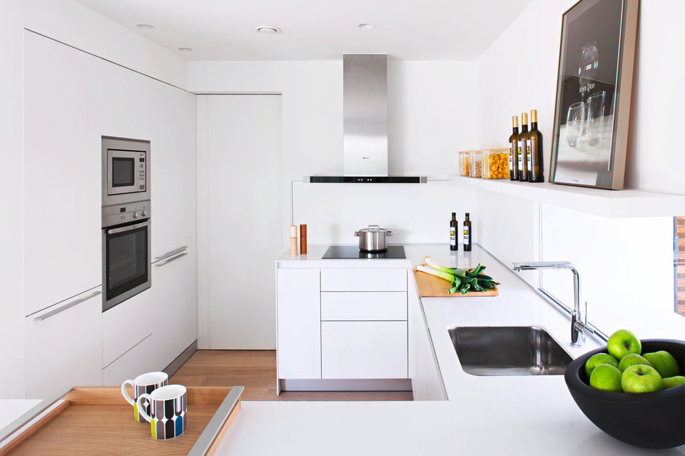 Design ideas for a small contemporary u-shaped enclosed kitchen in Munich with an integrated sink, flat-panel cabinets, white cabinets, composite countertops, white splashback, stainless steel appliances, medium hardwood flooring and no island.