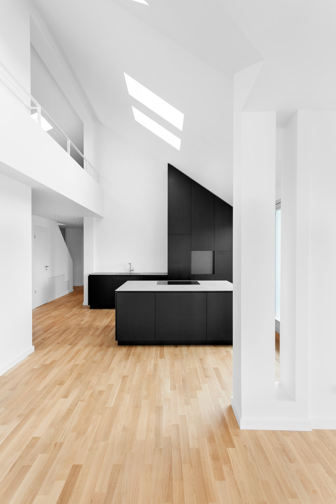 Идея дизайна: огромная кухня-гостиная в современном стиле с плоскими фасадами, черными фасадами, белым фартуком, островом и светлым паркетным полом