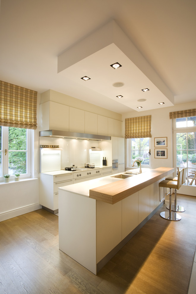 Design ideas for a medium sized traditional single-wall open plan kitchen in Cologne with a submerged sink, flat-panel cabinets, white cabinets, white splashback, glass sheet splashback, integrated appliances, medium hardwood flooring, an island and brown floors.