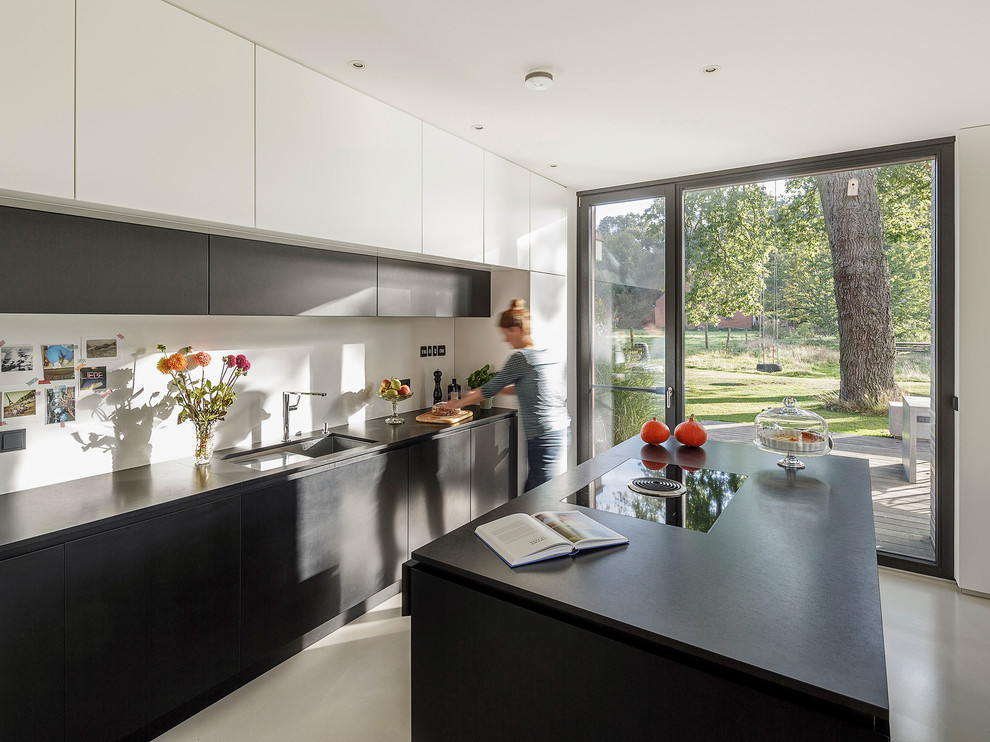 Inspiration for a mid-sized contemporary galley vinyl floor and gray floor open concept kitchen remodel in Cologne with an integrated sink, flat-panel cabinets, black cabinets, white backsplash, black appliances, an island and black countertops