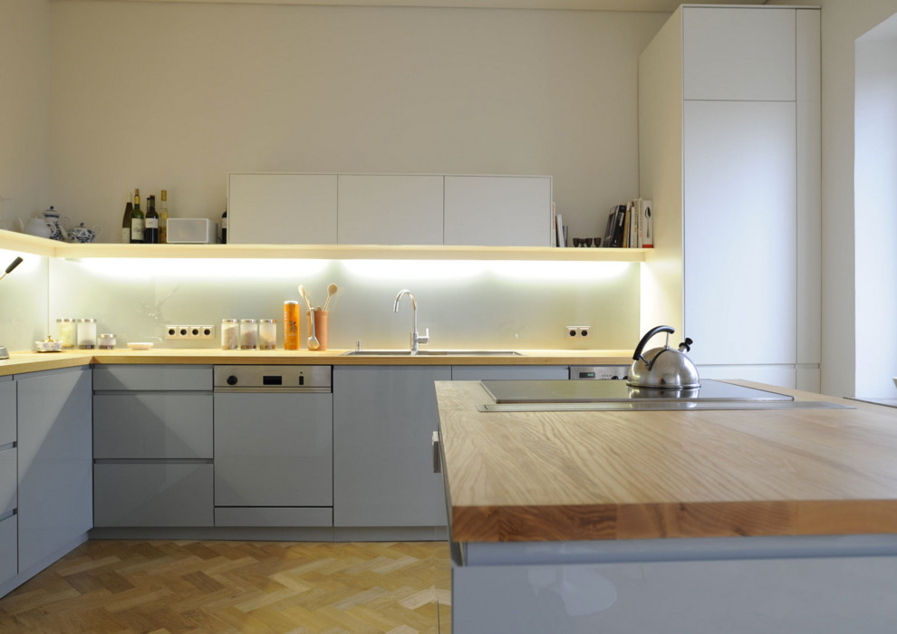 Bild på ett mycket stort funkis kök, med en dubbel diskho, släta luckor, grå skåp, träbänkskiva, vitt stänkskydd, glaspanel som stänkskydd, integrerade vitvaror, mellanmörkt trägolv och en köksö
