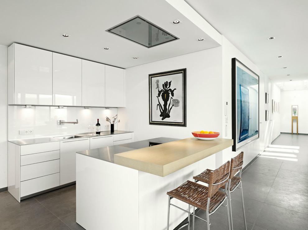 Photo of a small contemporary single-wall open plan kitchen in Cologne with an integrated sink, flat-panel cabinets, white cabinets, stainless steel worktops, white splashback, glass sheet splashback and an island.