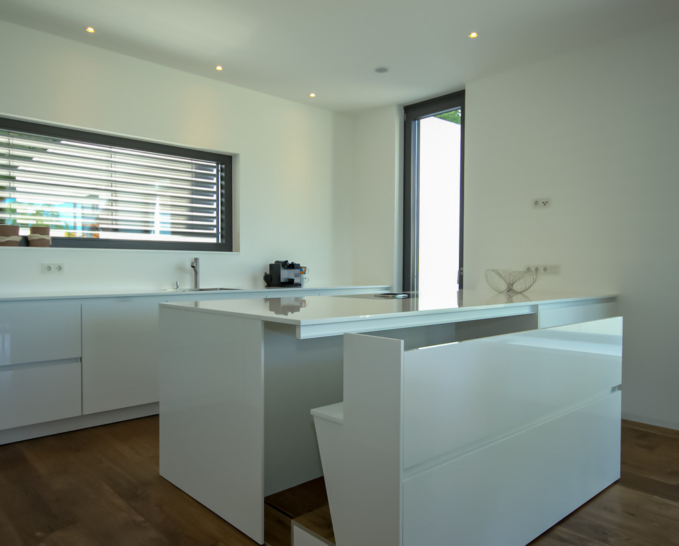 Large modern galley kitchen/diner in Other with a built-in sink, flat-panel cabinets, white cabinets, engineered stone countertops, white splashback, limestone splashback, stainless steel appliances, medium hardwood flooring, a breakfast bar, brown floors and white worktops.