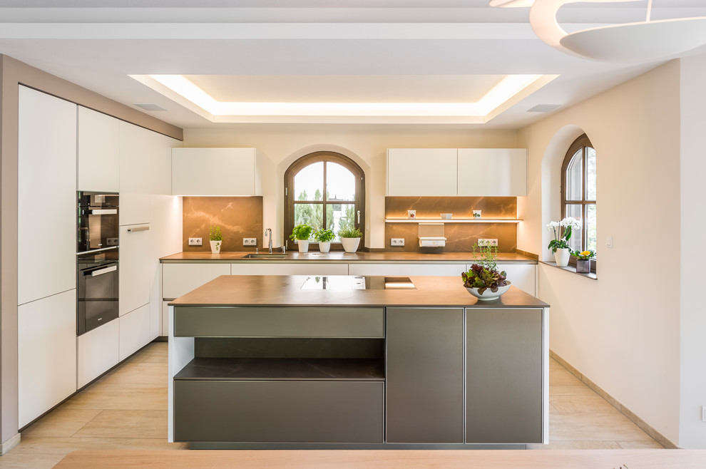 Idéer för att renovera ett stort funkis linjärt kök med öppen planlösning, med en undermonterad diskho, släta luckor, vita skåp, bänkskiva i koppar, brunt stänkskydd, stänkskydd i keramik, svarta vitvaror, kalkstensgolv, en köksö och beiget golv