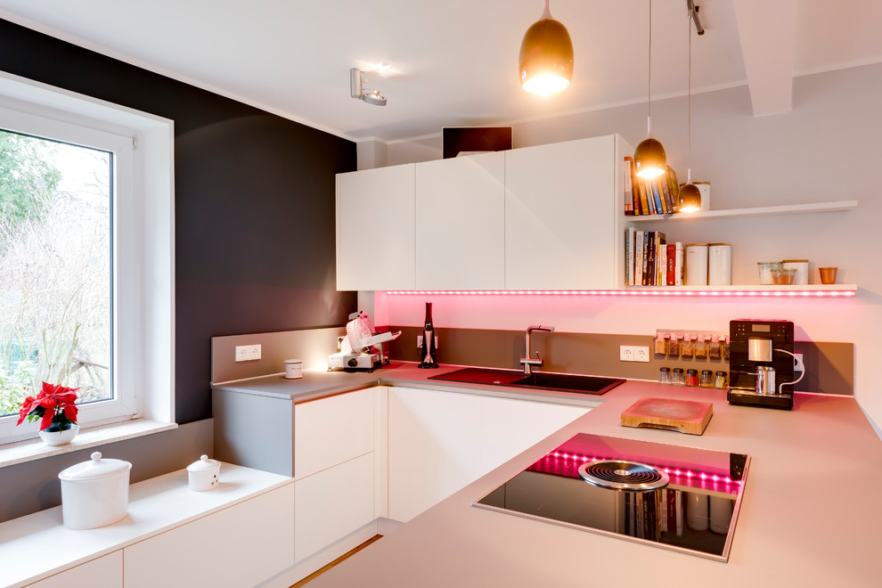 Medium sized contemporary u-shaped open plan kitchen in Hamburg with a built-in sink, flat-panel cabinets, white cabinets, composite countertops, stone slab splashback, black appliances, light hardwood flooring, a breakfast bar, brown floors and grey worktops.