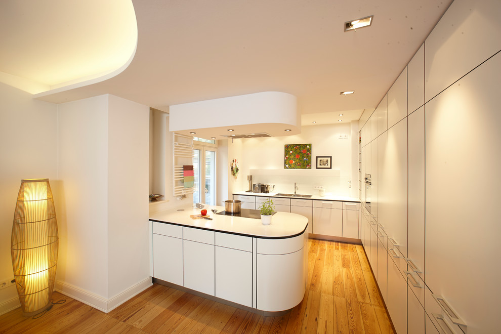 This is an example of a large contemporary l-shaped open plan kitchen in Hamburg with a double-bowl sink, flat-panel cabinets, white cabinets, composite countertops, white splashback, glass sheet splashback, integrated appliances, medium hardwood flooring and a breakfast bar.