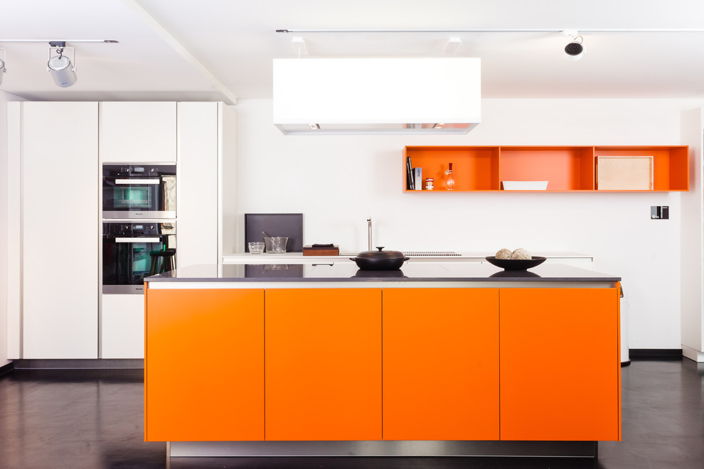 Foto de cocina actual grande con armarios con paneles lisos, puertas de armario naranjas, suelo de cemento, una isla y electrodomésticos de acero inoxidable