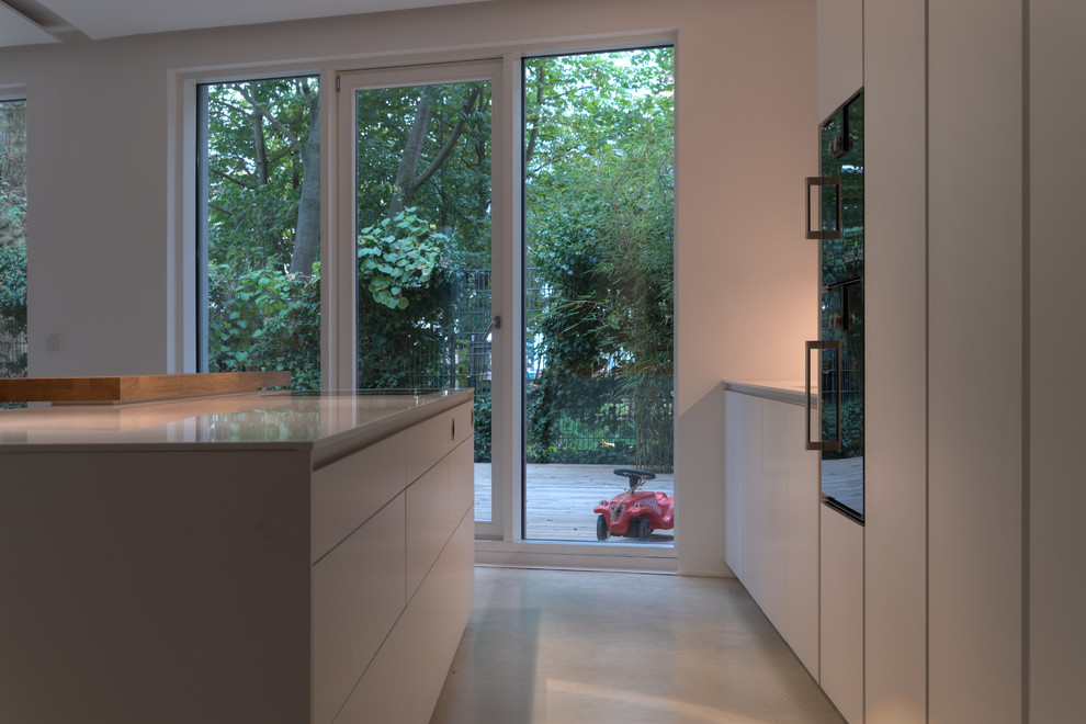 Foto di una cucina minimal di medie dimensioni con lavello sottopiano, ante lisce, ante bianche, top in superficie solida, paraspruzzi bianco e elettrodomestici neri