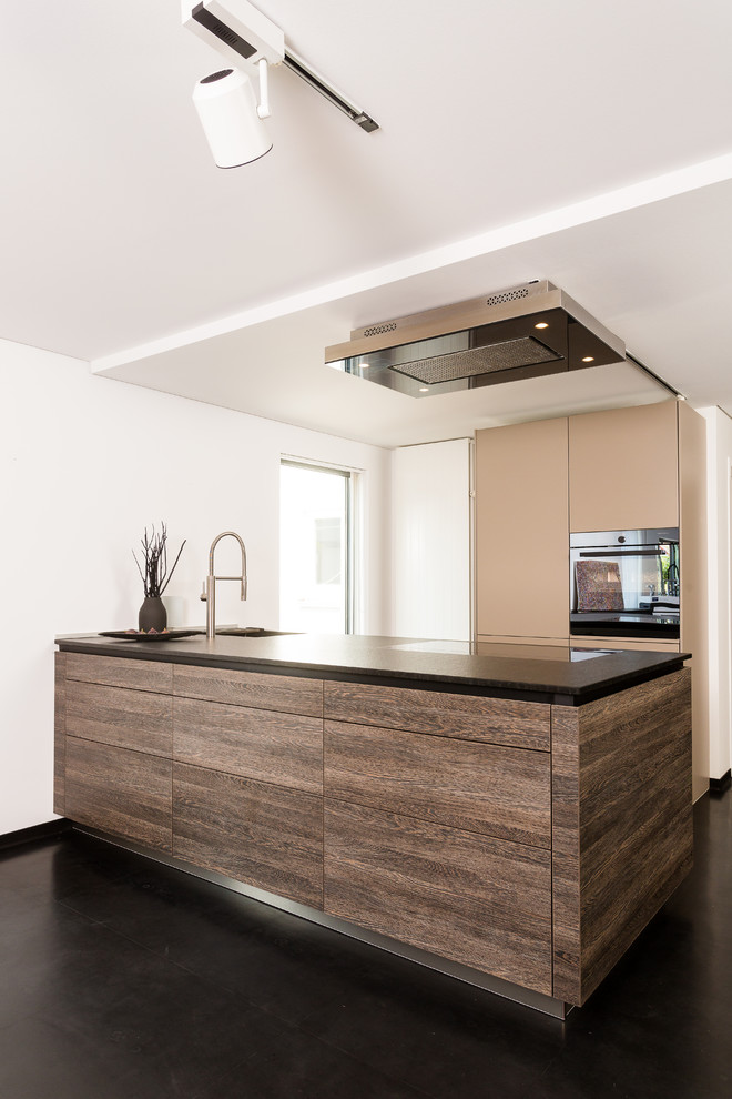 Esempio di una piccola cucina minimal con lavello sottopiano, ante lisce, ante in legno bruno, top in granito, elettrodomestici neri, pavimento nero e top nero