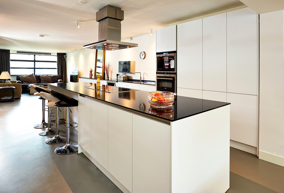 Идея дизайна: большая прямая кухня-гостиная в современном стиле с накладной мойкой, плоскими фасадами, белыми фасадами, гранитной столешницей, черной техникой и островом