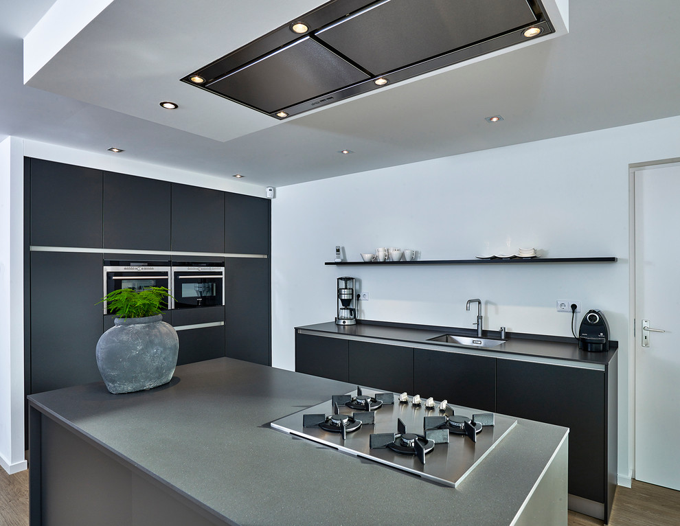 Immagine di una cucina contemporanea di medie dimensioni con lavello da incasso, ante lisce, ante grigie, top in quarzo composito, elettrodomestici neri e pavimento in legno massello medio