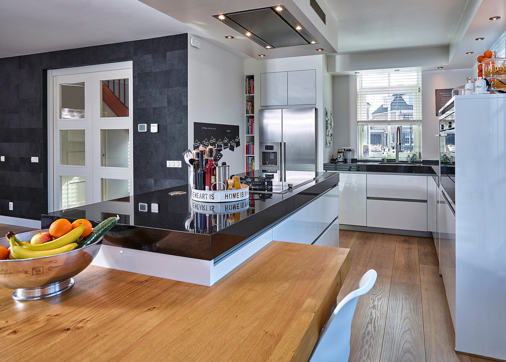 Bild på ett mellanstort funkis kök, med släta luckor, vita skåp, rostfria vitvaror, ljust trägolv, en köksö, en nedsänkt diskho och vitt stänkskydd