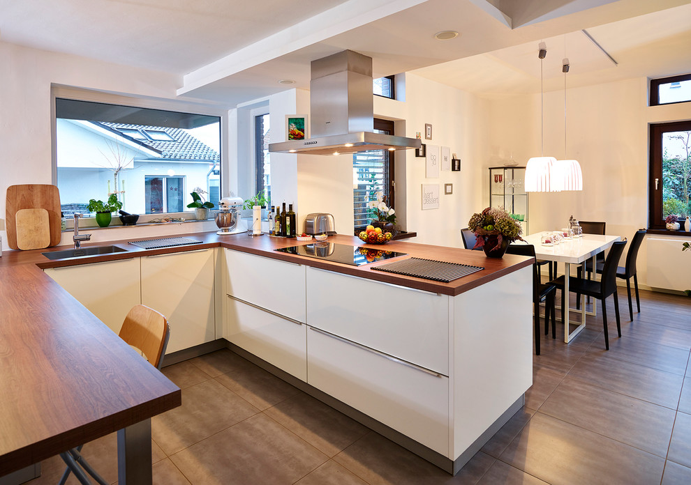 Immagine di una cucina design di medie dimensioni con ante lisce, ante bianche, elettrodomestici in acciaio inossidabile, penisola, top in legno, lavello da incasso e paraspruzzi bianco